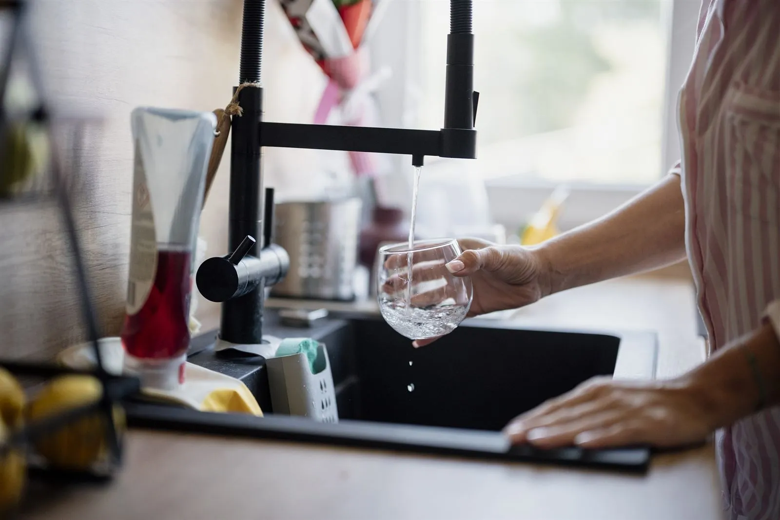 A person filling a glass with water from a black kitchen tap