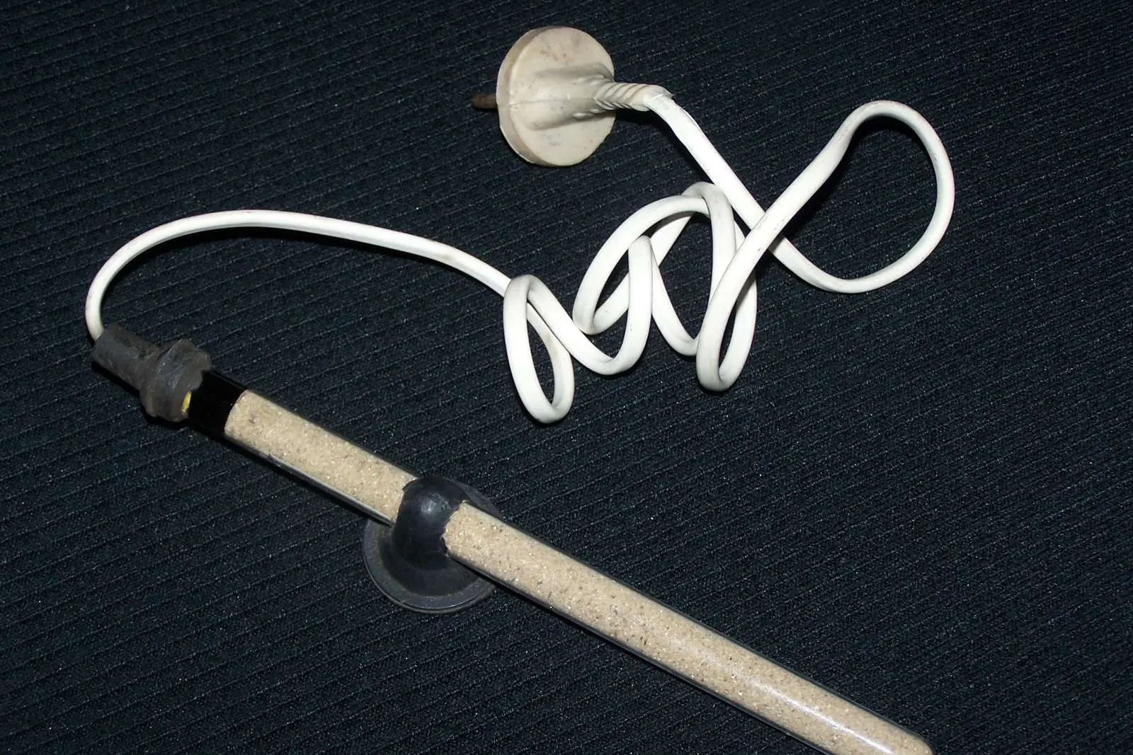 A glass aquarium heater with suction cups and a coiled white cable on a dark background