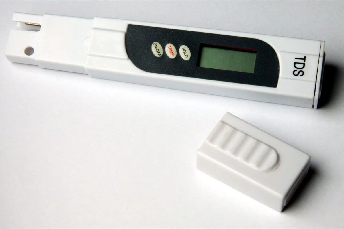 A white pen-style TDS meter with its cap off, lying on a white surface